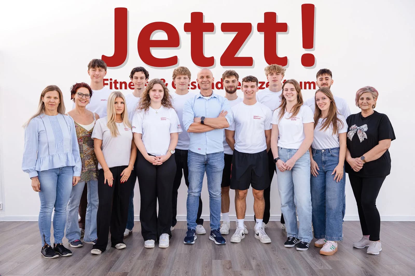 Das Team des JETZT! Fitness- und Gesundheitszentrums vor der Wand mit dem Jetzt!-Schriftzug